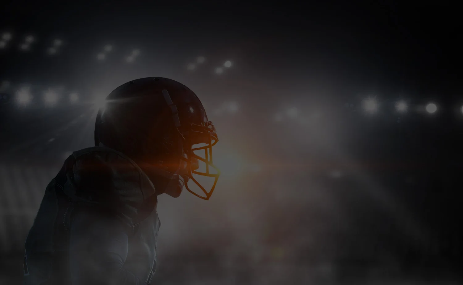 A football player in a dark setting, highlighted by bright lights, showcasing focus and determination
